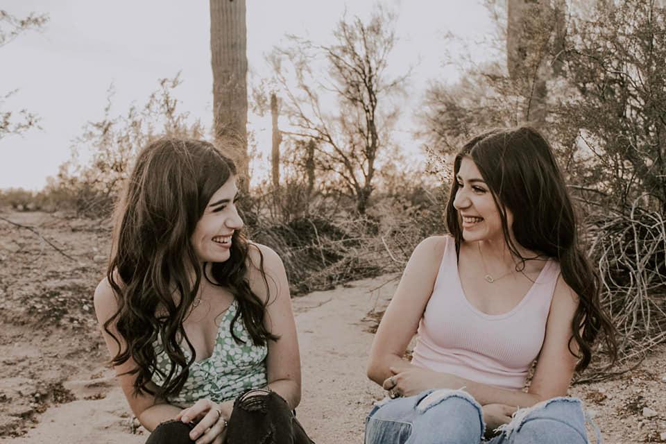 twin girls facing each other laughing outside in the desert, one in a pink shirt, one in a green shirt