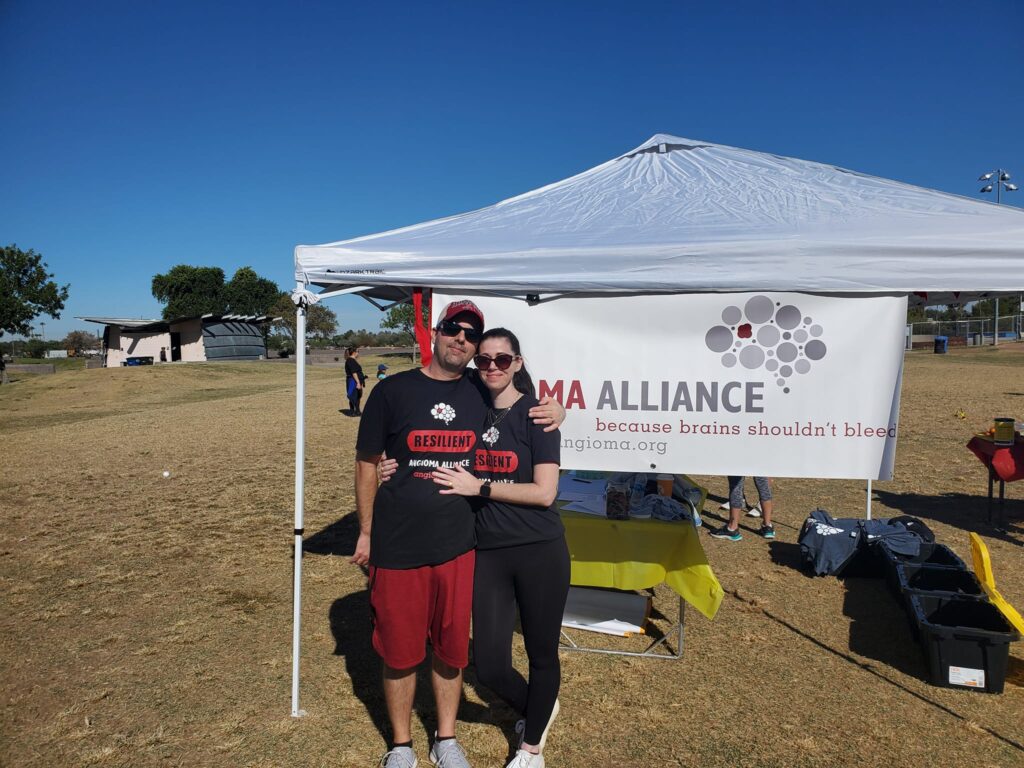 a couple wearing matching back shirt with the word 'Reslient' on them outside in front of a white tent and banner