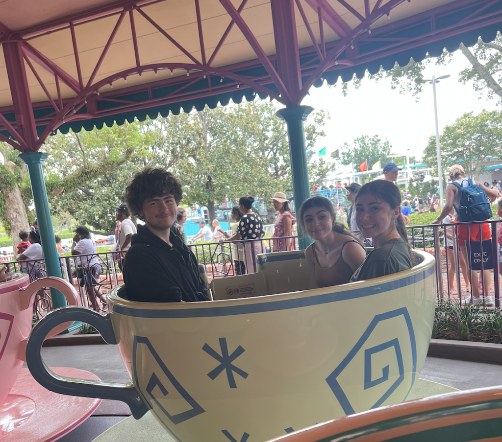 two girls and a boy sitting in a teacup at an amusement park smiling 